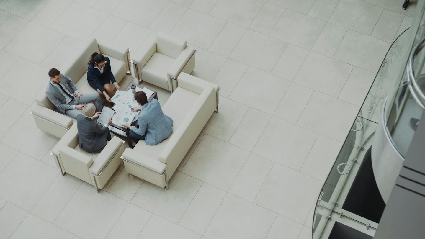 Cztery osoby w lobby biurowym przeglądają dokumenty przy stole.
